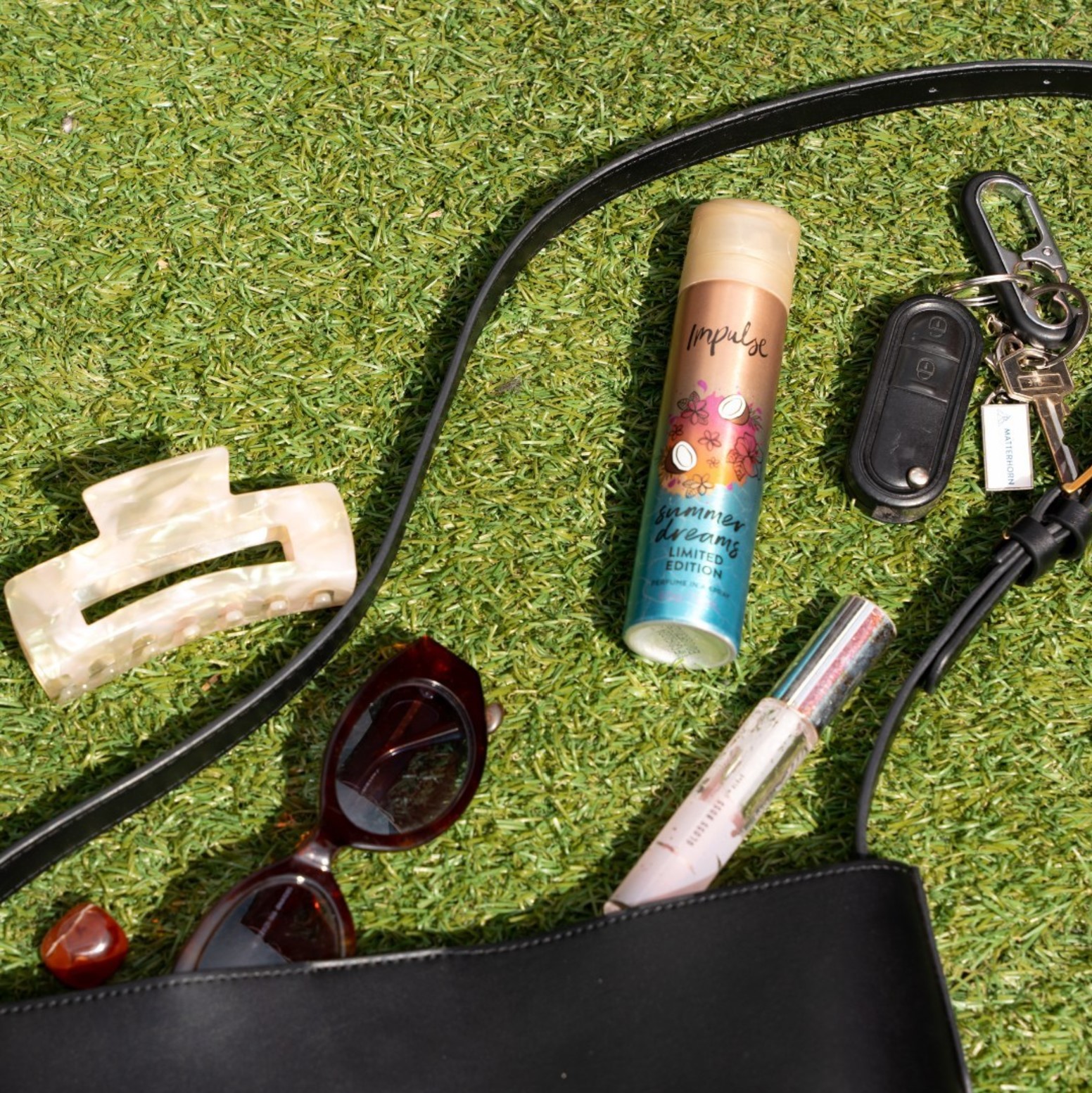 Impulse body spray on the grass surrounded by car keys, handbag, lip balm and hair clip